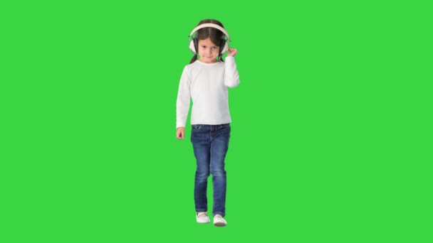 Egy fehér ruhás kislány, aki fejhallgatóban sétál és bólogat a zenére, amit egy zöld vásznon, Chroma Key-n énekel.. — Stock videók