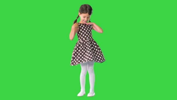 Gülümseyen küçük kız poz veriyor ve benekli elbisesini yeşil ekranda çeviriyor, Chroma Key. — Stok video