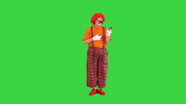 Payaso divertido mirando el teléfono inteligente y reaccionando a lo que ve en una pantalla verde, Chroma Key. — Vídeos de Stock