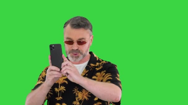 Modent mannlig turist i sommerklær som går og lager bilder med telefonen på en grønn skjerm, Chroma Key. – stockvideo