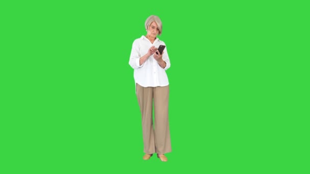 Стильная зрелая женщина, печатающая смс на мобильном телефоне на зеленом экране, Chroma Key. — стоковое видео