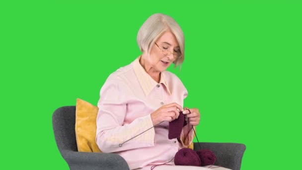 Ώριμη γιαγιά που κάθεται και πλέκει και λέει μια ιστορία στην κάμερα σε μια πράσινη οθόνη, Chroma Key. — Αρχείο Βίντεο