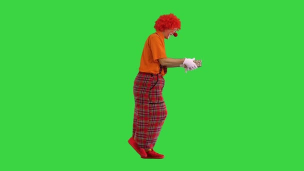 Un payaso macho feliz sosteniendo un regalo y caminando en una pantalla verde, Chroma Key. — Vídeo de stock