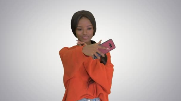 Smiling african american woman in bright jumper taking selfie and checking her phone on gradient background. — Stock Video