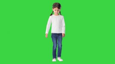 Uzun kollu beyaz gömlek giyen, kot pantolon giyen yeşil ekran Chroma Key 'de yürüyen ve kameraya bakan küçük kız..