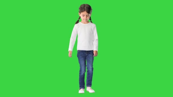 Κοριτσάκι με ουρές γουρουνιών ντυμένο με λευκό μακρυμάνικο μπλουζάκι και τζιν με τα πόδια και κοιτάζοντας την κάμερα σε μια πράσινη οθόνη, Chroma Key. — Αρχείο Βίντεο