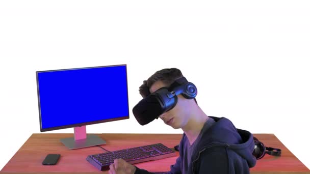 Giovane giocatore in realtà virtuale auricolare seduto a tavola su sfondo bianco. — Video Stock