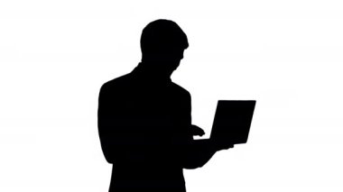 Siluet. Gülümseyen genç işadamı ayakta dururken dizüstü bilgisayar kullanıyor..