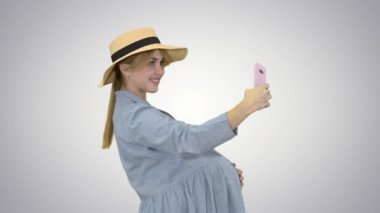 Çekici, şapkalı hamile bir kadın gradyan arka planda selfie çekiyor..