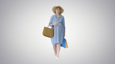 Hamile bir kadın yaz kıyafetleri içinde alışveriş torbalarıyla yürüyor..