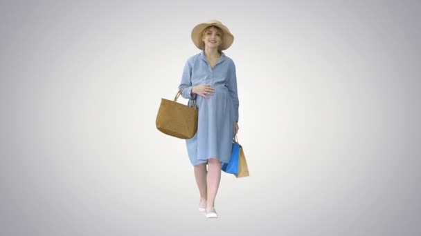 Femme enceinte en vêtements d'été marchant avec des sacs à provisions sur fond de dégradé. — Video
