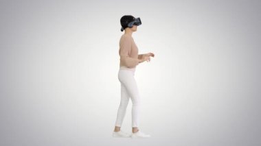 Arkaplanda yürüyen ve etkileşimli VR kulaklık kullanan sevimli genç bir kadın..
