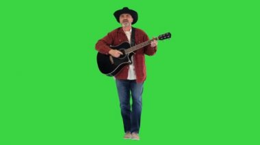 Yaşlı kovboy yürür, şarkı söyler ve gitar çalar Yeşil Ekran, Chroma Key 'de.
