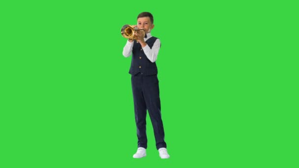 Kleine jongen in een strikje spelen van de trompet en kijken naar de camera op een groen scherm, Chroma Key. — Stockvideo