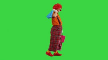 Yeşil Ekran 'da alışveriş torbalarıyla yürüyen komik bir palyaço, Chroma Key.