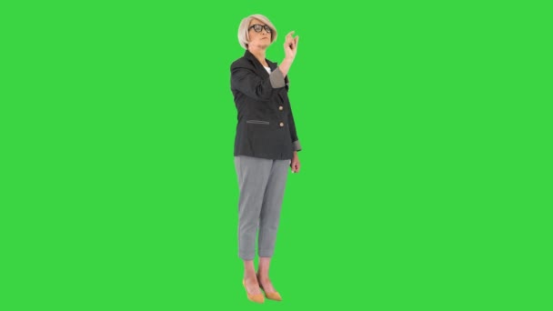 Mujer de negocios senior con gafas apuntando a los botones de una pantalla virtual en una pantalla verde, Chroma Key. — Vídeo de stock