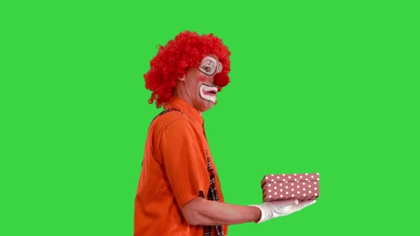 Clown trägt eine Geschenkschachtel und schaut auf einem Green Screen hinein, Chroma Key. — Stockvideo