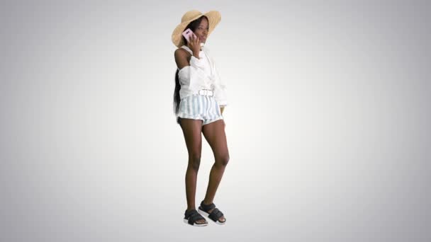 Bastante joven afroamericana mujer en un sombrero de paja hablando en su teléfono sobre fondo degradado. — Vídeos de Stock