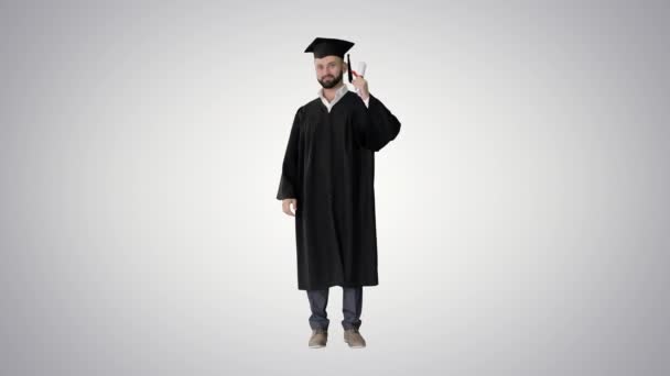 Щасливий студент носить випускний халат і тримає свій сертифікат і піднімає великий палець на градієнтному фоні . — стокове відео