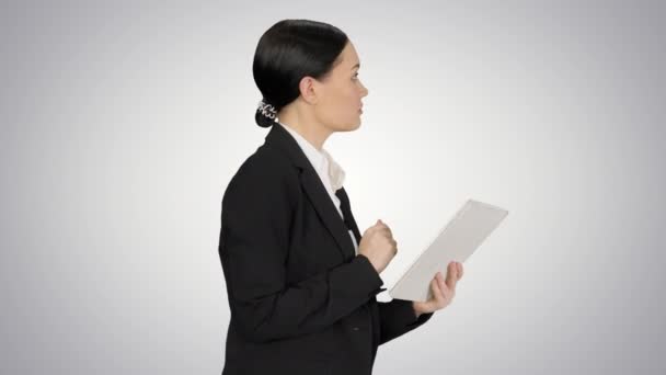 Businesswoman using a tablet pad while walking on gradient background. — Stock Video