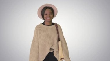 Örgü ve beyaz şapkalı gülümseyen Afro-Amerikan kadın arka planda yürürken poz veriyor..
