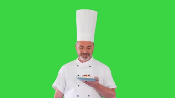 Lo chef maturo, il cuoco o il fornaio tiene il piatto con il dessert e fa il gesto di approvazione su uno schermo verde, chiave del cromo. — Video Stock