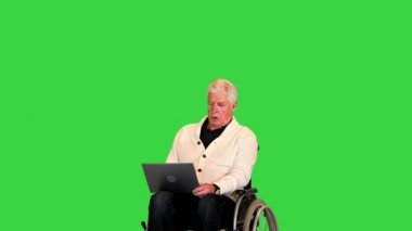 Tekerlekli sandalyedeki engelli yaşlı adam yeşil ekran, Chroma Key 'de dizüstü bilgisayarda yazıyor..