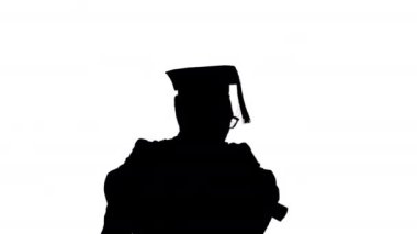 Siluet Heyecanlı Afro-Amerikan erkek öğrenci mezuniyet cübbesi içinde diplomasıyla mutlu bir şekilde dans ediyor..