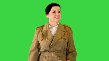 Trençkotlu olgun bir kadın yeşil ekranda alışveriş torbalarıyla yürüyor, Chroma Key..