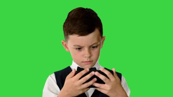 Ένα μικρό αγόρι με γιλέκο να βλέπει κάτι στο κινητό του και να γυρίζει τα μάτια του σε κατάσταση σοκ σε μια πράσινη οθόνη, το Chroma Key. — Αρχείο Βίντεο