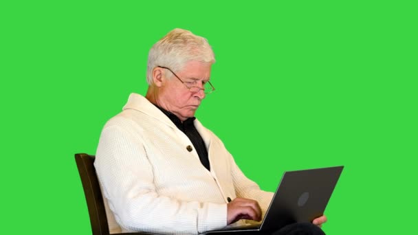 Vieil homme assis dans un fauteuil à l'aide d'un ordinateur portable sur un écran vert, Chroma Key. — Video