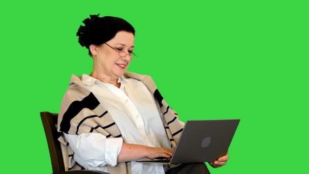 Senior vrouw zitten in stoel en werken aan laptop op een groen scherm, Chroma Key. — Stockvideo