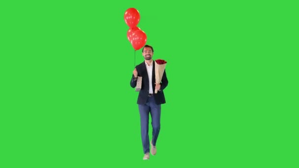 Elegant man, in a suit, with a bouquet of flowers, a gift and balloons walking on a Green Screen, Chroma Key. — Stock Video