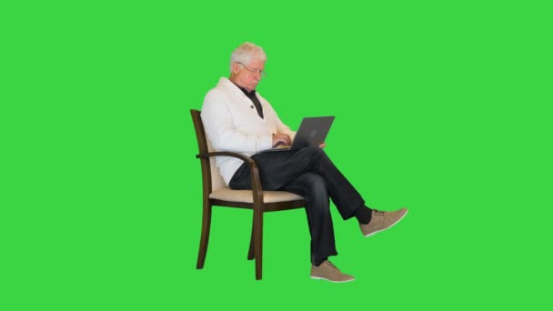 Alter Mann sitzt im Sessel mit Laptop-Computer auf einem grünen Bildschirm, Chroma Key. — Stockvideo