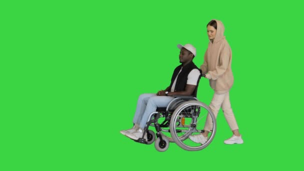 Caucasian lady pushes her disabled friend and leaves him waiting on a Green Screen, Chroma Key. — Stock Video
