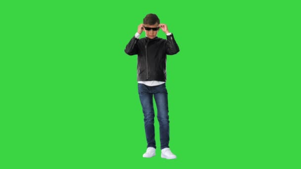 Niño en una chaqueta de cuero que se pone gafas negras con brazos en las caderas en una pantalla verde, Chroma Key. — Vídeo de stock