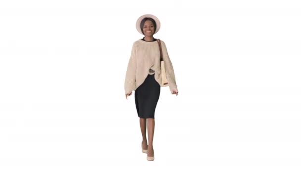 Улыбающаяся африканская американка в трикотаже и в белой шляпе позирует во время прогулки на белом фоне. — стоковое видео