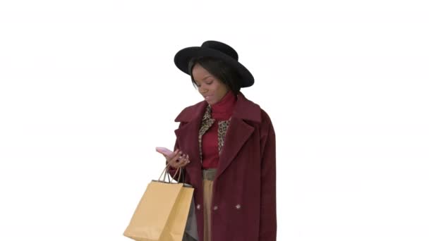 Uśmiechnięta Afroamerykanka dziewczyna moda w płaszczu i czarny kapelusz smsowanie na jej telefon na białym tle. — Wideo stockowe