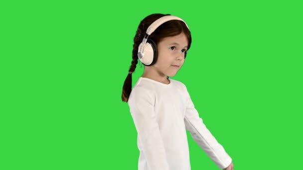 Izgatott kislány fehér ruhában hallgatja a zenét fülhallgatóban és énekel együtt a zöld képernyőn, Chroma Key. — Stock videók