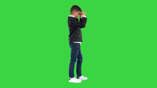 Niño en una chaqueta de cuero que se pone gafas negras con brazos en las caderas en una pantalla verde, Chroma Key. — Vídeo de stock