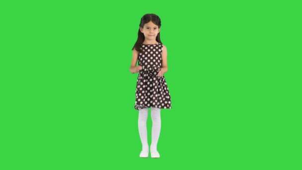 Dunkelhaariges kleines Mädchen im gepunkteten Kleid, das eine schwarze Sonnenbrille auf einem Green Screen aufsetzt, Chroma Key. — Stockvideo