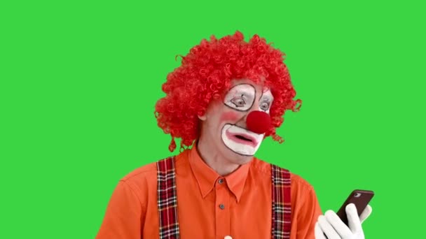 Clown divertente guardando smartphone e reagendo su ciò che vede su uno schermo verde, Chroma Key. — Video Stock