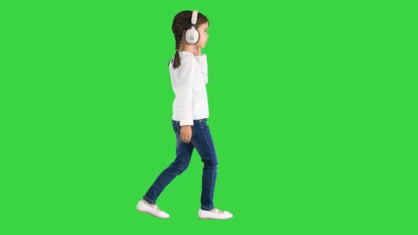 Κοριτσάκι ντυμένο στα λευκά περπατώντας με ακουστικά και κουνώντας το κεφάλι της στο ρυθμό της μουσικής σε μια πράσινη οθόνη, Chroma Key. — Αρχείο Βίντεο