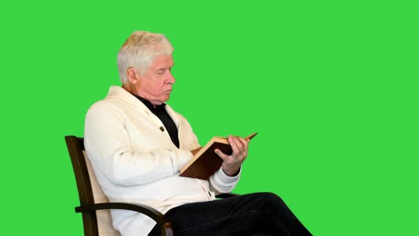 Ανώτερος άνθρωπος μελετώντας ένα βιβλίο κάθεται σε μια καρέκλα σε μια πράσινη οθόνη, Chroma Key. — Αρχείο Βίντεο
