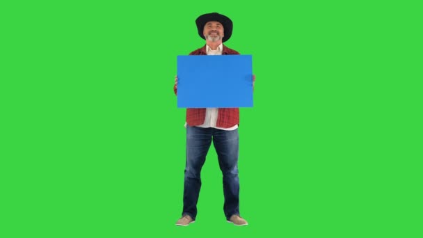 Kovboy şapkalı çiftçi boş tahtayla duruyor ve yeşil ekrandaki kameraya gülümsüyor, Chroma Key.. — Stok video