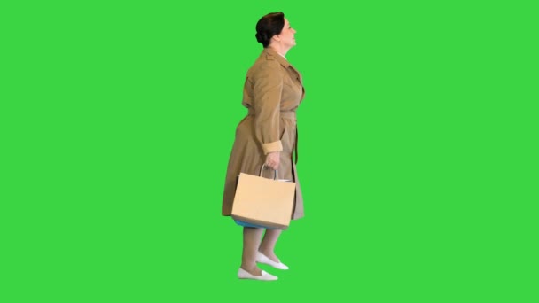 Зрелая женщина в плаще ходит с пакетами для покупок на зеленом экране, хрома ключ. — стоковое видео