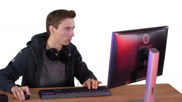 Геймер хлопець з навушниками грає у відеоігри на комп'ютері і показує великий палець до камери на білому тлі . — стокове відео