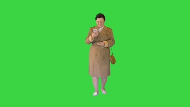 Kobieta w średnim wieku w płaszczu i za pomocą smartfona na zielonym ekranie, Chroma Key. — Wideo stockowe
