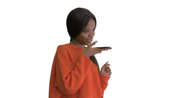 Pretty african american woman in bright jumper dictating message using her phone on white background. — Stock Video