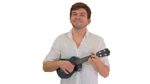 Pria muda tersenyum bermain ukulele melihat ke kamera pada latar belakang putih. — Stok Video